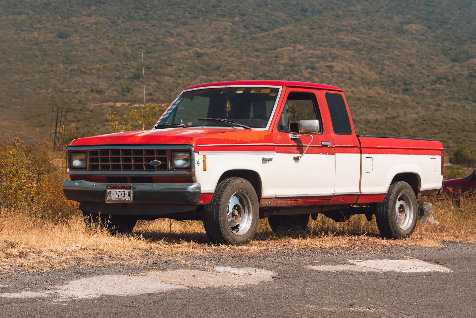 A vintage red and white pickup truck parked on a roadside in La Yerbabuena, Mexico.